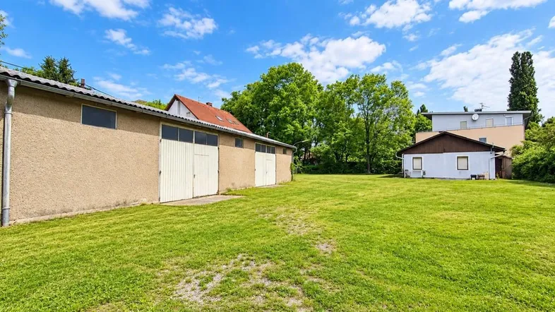 Große Rasenfläche mit mehreren Gebäuden im Hintergrund unter blauem Himmel mit Wolken.