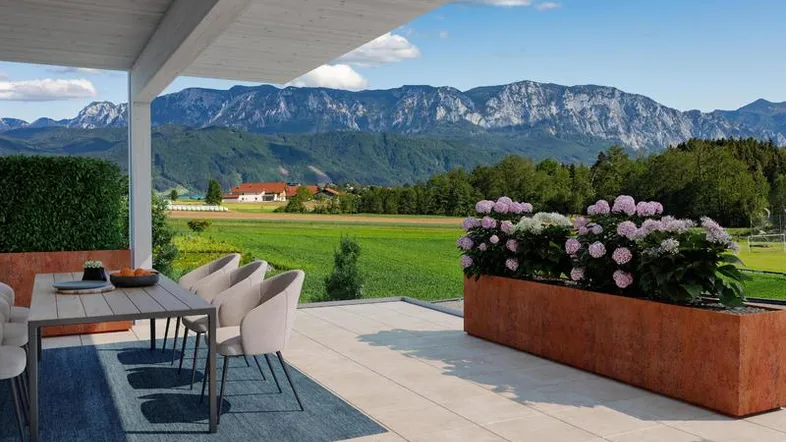 Überdachte Terrasse mit Esstisch, Pflanzen und weitem Blick auf die Berge und grüne Felder.