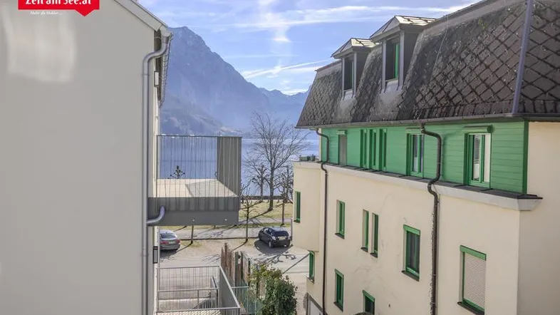 Blick zwischen Gebäuden auf eine Straße, den See und die beeindruckende Berglandschaft im Hintergrund.