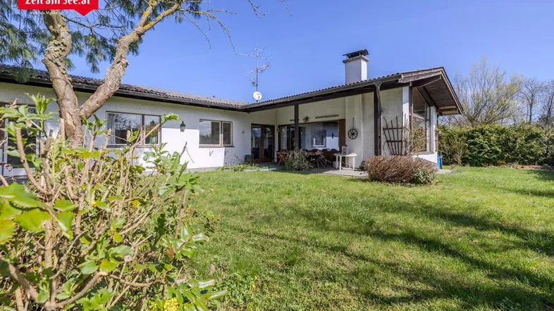 Rückansicht des Hauses mit Terrasse und weitläufigem Gartenbereich unter blauem Himmel.