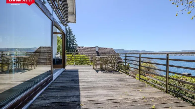 Geräumige Holzterrasse mit Esstisch und atemberaubendem Blick auf den See und die umliegende Landschaft.