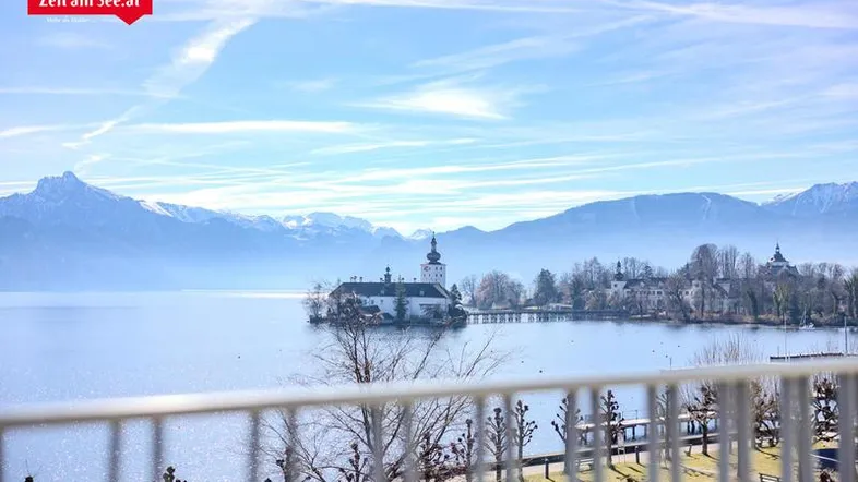 Panoramablick vom Balkon auf den See, ein Schloss und die umliegende Berglandschaft.