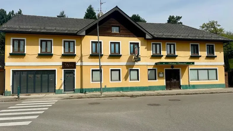 Gelbes Gebäude mit traditioneller Architektur, dunklem Dach und mehreren Fenstern an einer Straße gelegen.