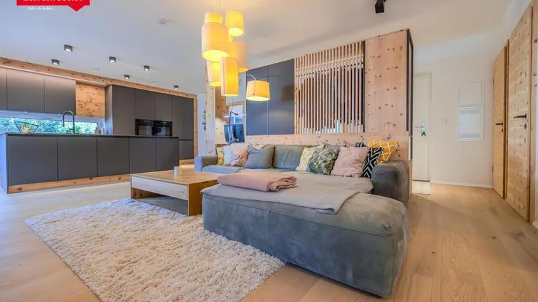 Helles Wohnzimmer mit bequemer Couch, Holzboden und Blick zur modernen Küche.