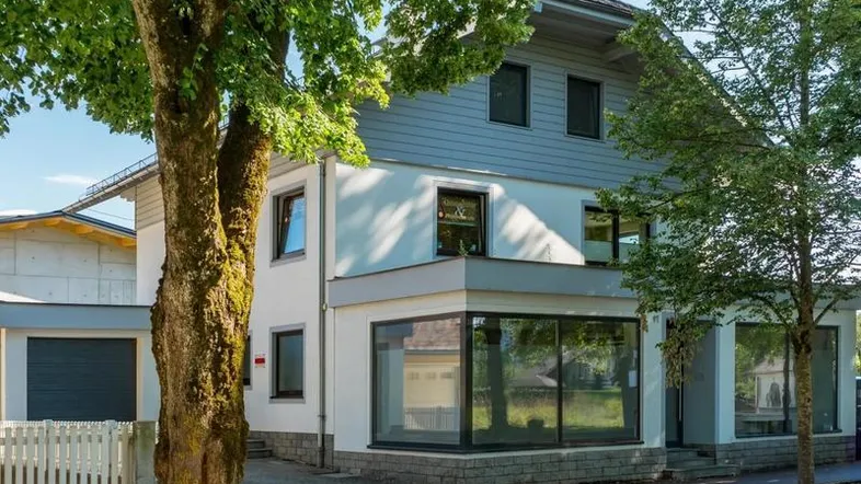 Modernes Wohnhaus mit großen Fenstern und umliegenden Bäumen in einer grünen Umgebung.