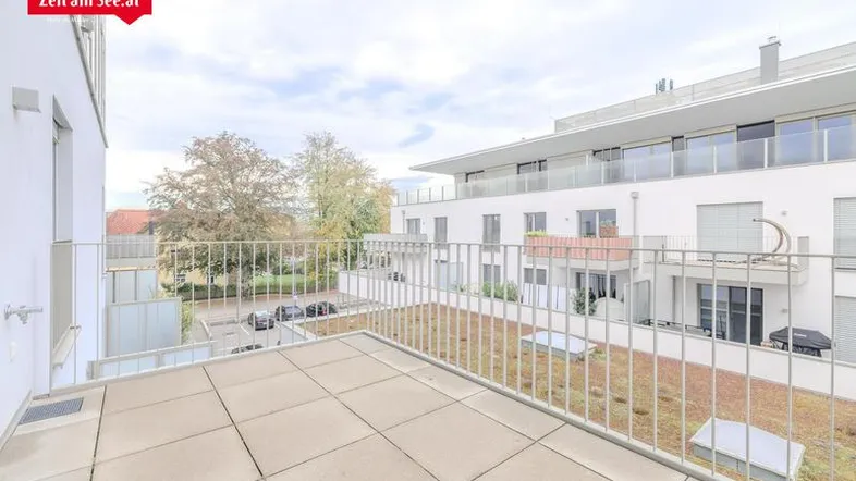 Geräumiger Balkon mit Fliesenboden und Blick auf die umliegenden Gebäude und eine begrünte Dachfläche.