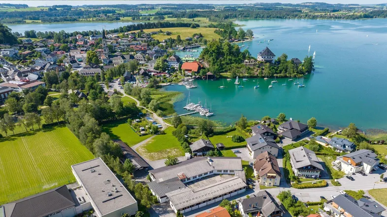 Luftaufnahme einer malerischen Stadt am Seeufer, umgeben von grünen Hügeln und Wäldern.