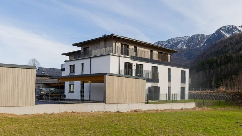 Modernes Mehrfamilienhaus mit Holzverkleidung, Carport und Bergblick in ländlicher Umgebung.
