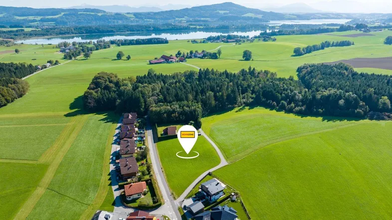 Luftaufnahme der ländlichen Umgebung mit See, grünen Feldern und Wohnsiedlung.