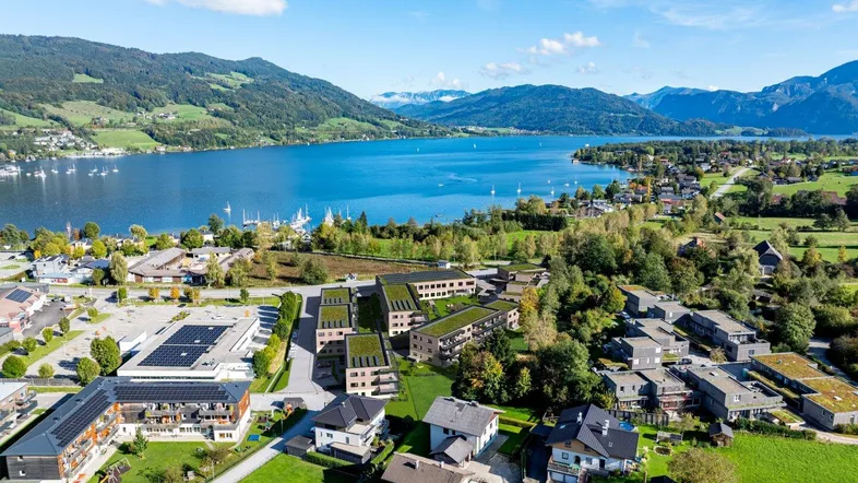 Luftaufnahme eines modernen Wohnkomplexes mit Gründächern und Seeblick in bergiger Landschaft.