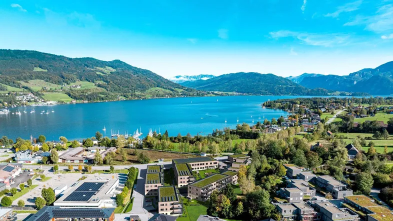 Panoramablick auf die moderne Wohnanlage am Seeufer mit umliegender Berglandschaft.