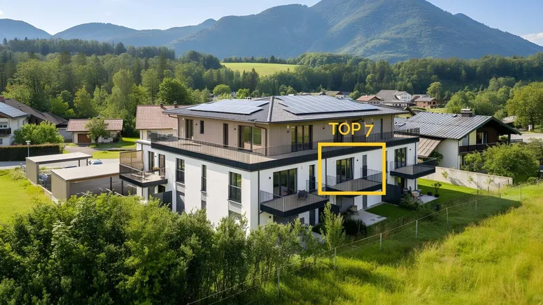 Modernes Mehrfamilienhaus mit Balkonen, Photovoltaikanlage und Bergblick in grüner Umgebung.