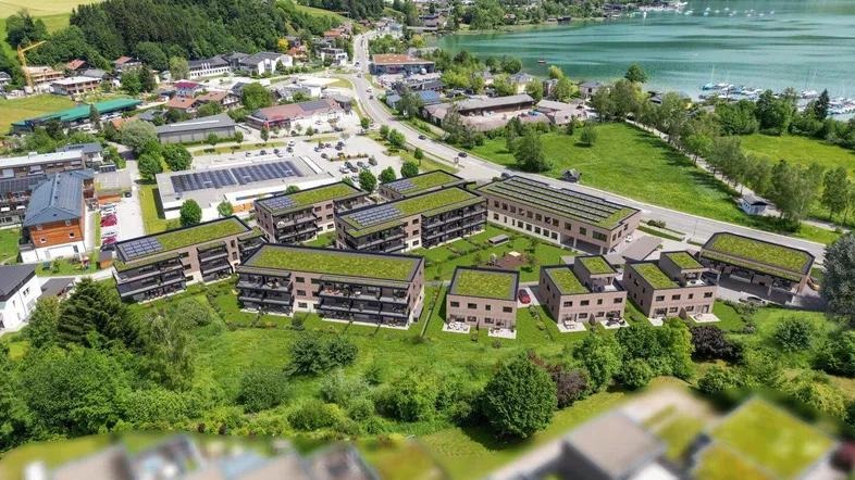 Luftaufnahme einer modernen Wohnanlage mit begrünten Dächern, umgeben von Natur, See und Bergen.