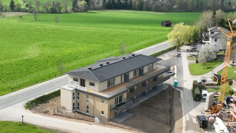 Neues Mehrfamilienhaus in ländlicher Umgebung mit Blick auf grüne Hügel und See, umgeben von Natur.