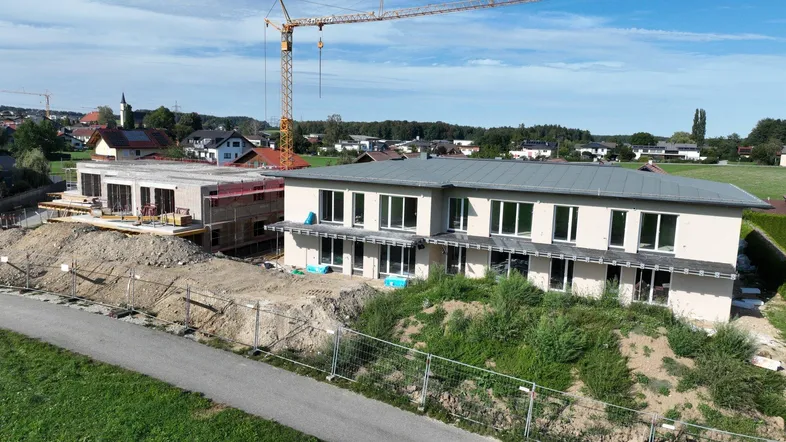 Luftaufnahme eines Neubauprojekts mit zwei Gebäuden in unterschiedlichen Bauphasen und einem Kran.