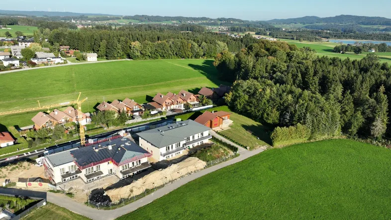 Luftaufnahme eines Neubauprojekts mit mehreren Gebäuden, umgeben von grünen Feldern und Wäldern.