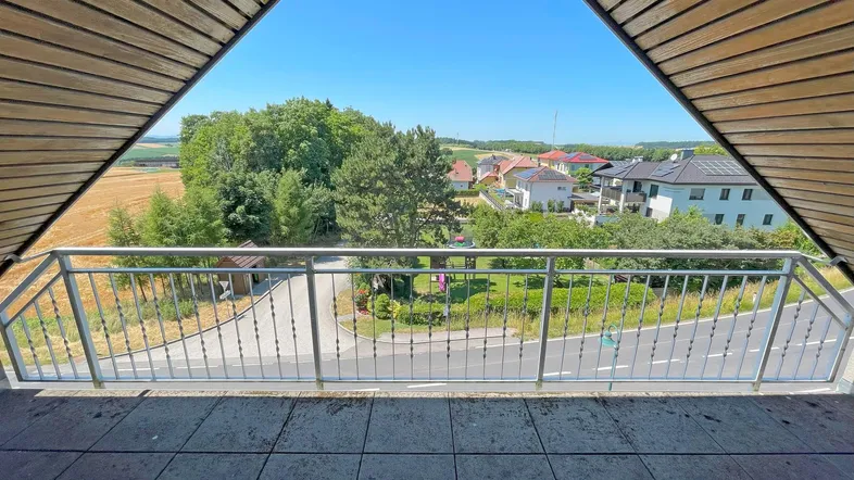 Geräumiger Balkon mit Holzdach und weitem Blick über die Landschaft und umliegende Häuser.
