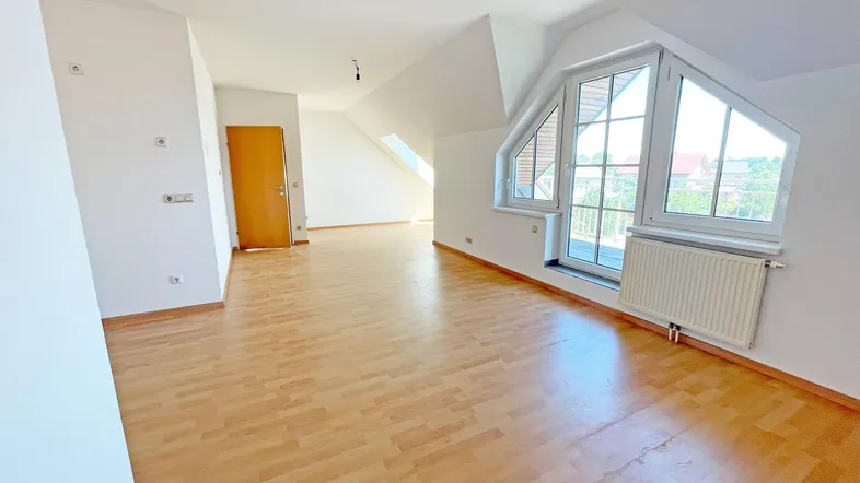 Heller, leerer Wohnbereich im Dachgeschoss mit Laminatboden und großen Fenstern.