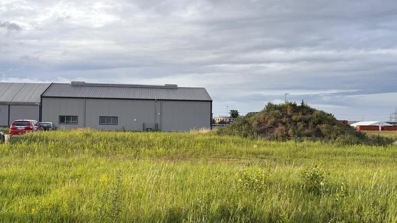 Weitläufiges Grasfeld mit einem modernen Industriegebäude im Hintergrund unter bewölktem Himmel.
