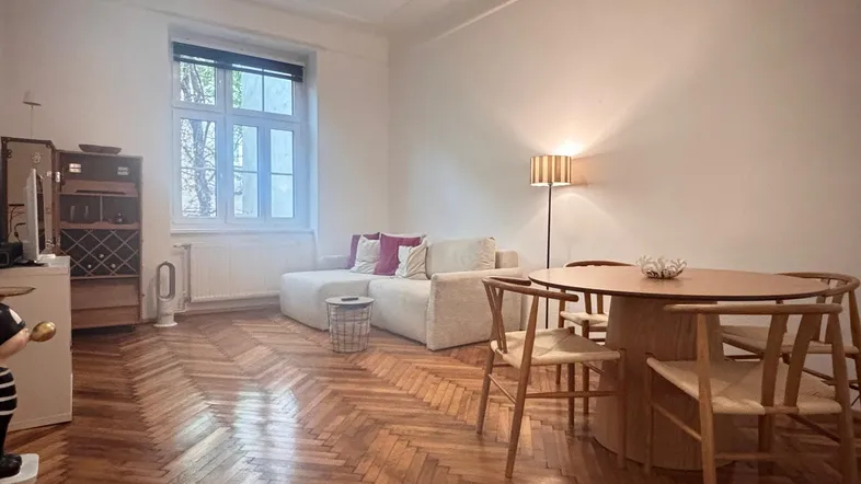 Heller Wohn- und Essbereich mit Fischgrätparkett, bequemer Couch und einem Esstisch am Fenster.