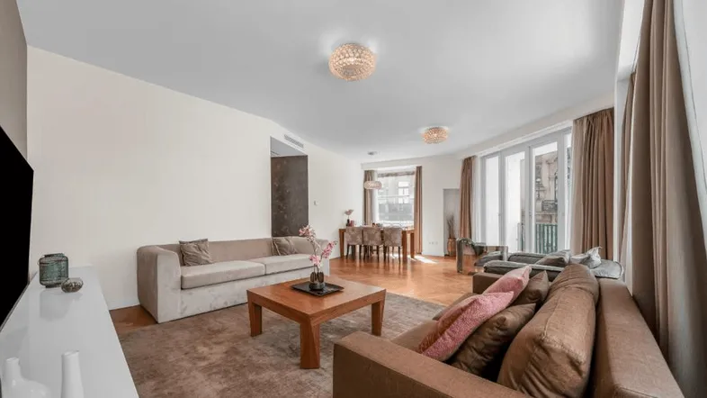Geräumiger Wohn- und Essbereich mit elegantem Fischgrätparkett, bequemen Sofas und Zugang zu einem französischen Balkon.