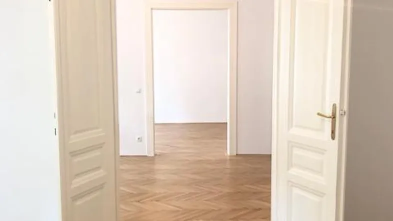 Heller Innenraum mit Fischgrätparkett und mehreren offenen Türen, die einen weiten Blick ermöglichen.