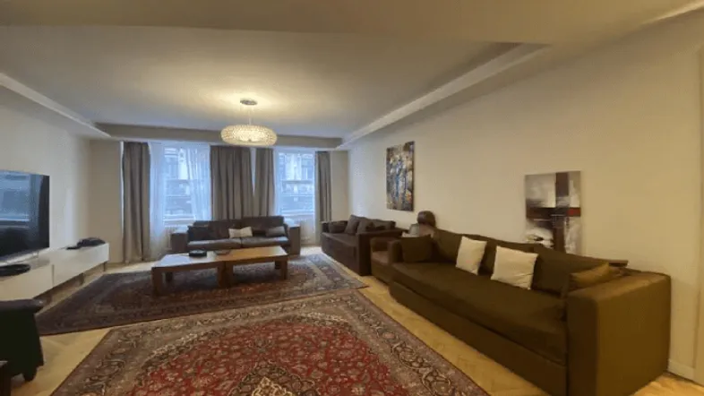 Großzügiges Wohnzimmer mit mehreren Sofas, orientalischem Teppich und viel Tageslicht.