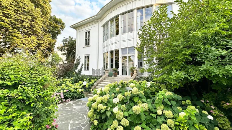 Elegante weiße Villa mit gepflegtem Vorgarten, blühenden Hortensien und Steinweg.