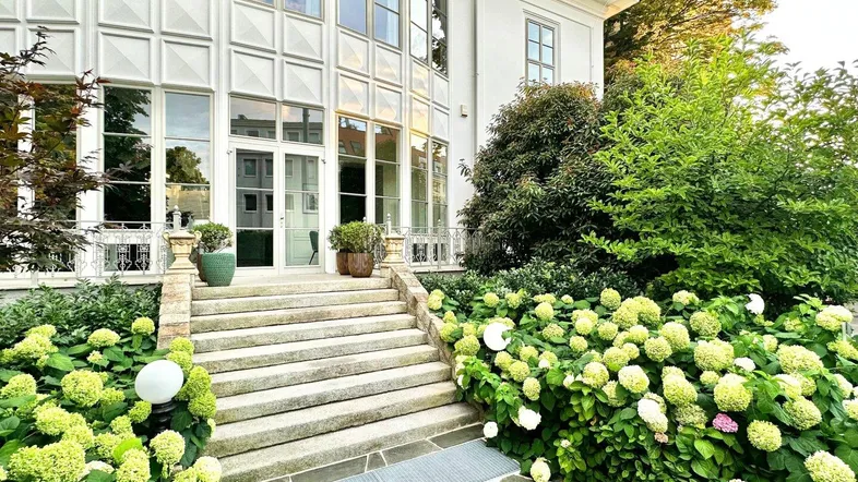 Elegante weiße Villa mit großen Fenstern und gepflegtem Vorgarten voller Hortensien.