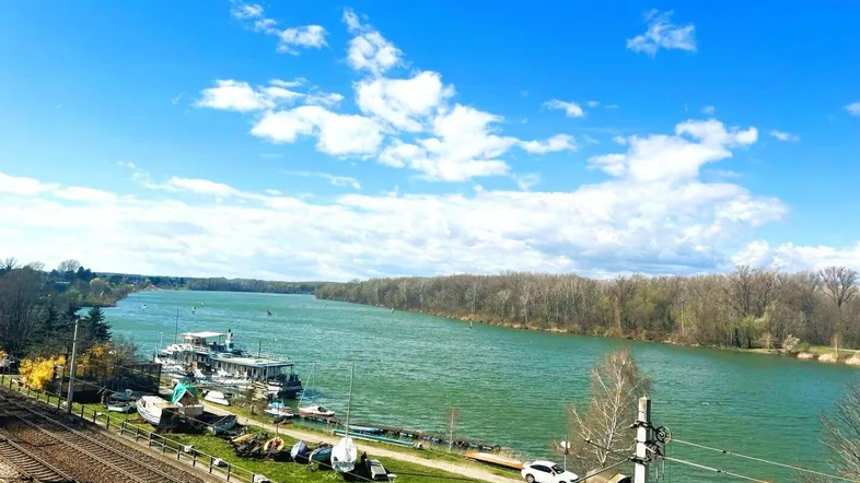 Panoramablick von der Terrasse auf den Fluss mit Booten und bewaldeten Ufern unter blauem Himmel.