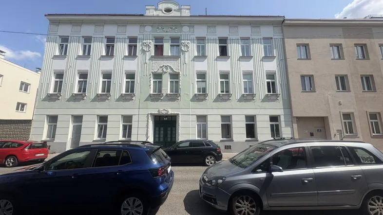 Historische Fassade eines Mehrfamilienhauses mit klassischer Architektur und parkenden Autos davor.