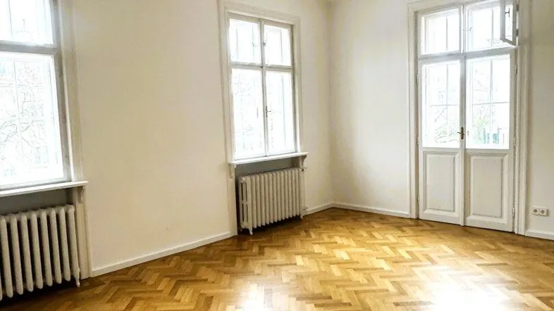 Helles Zimmer mit Fischgrätparkettboden, hohen Decken und Stuckverzierung an der Decke.