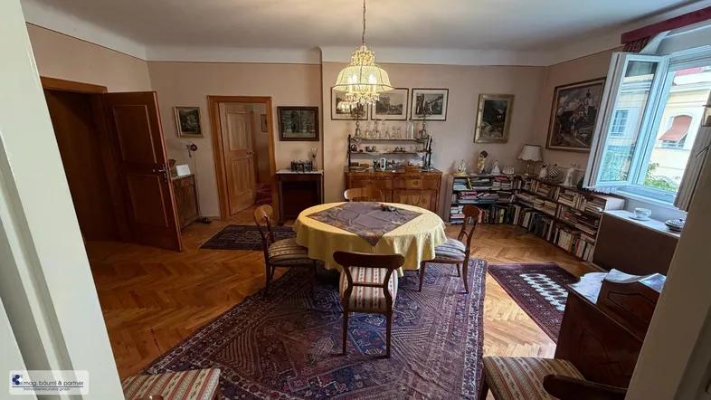 Geräumiges Esszimmer mit Fischgrätparkett, antiken Möbeln und einem großen Fenster.