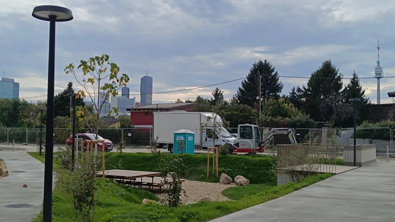 Blick auf eine Außenanlage mit Grünflächen, Baustelle und der Wiener Skyline im Hintergrund.