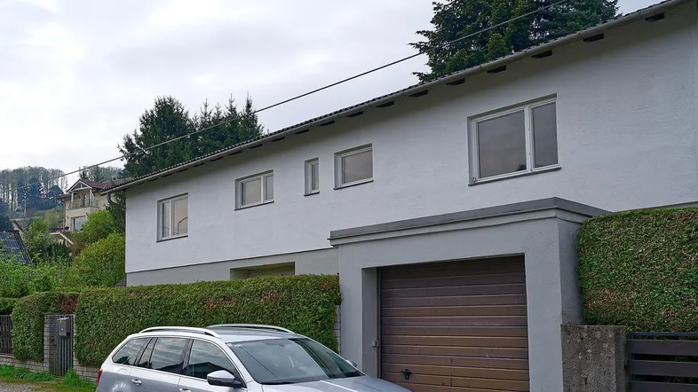 Ansicht der Hausfassade mit integrierter Garage und gepflegter Hecke im Vordergrund.