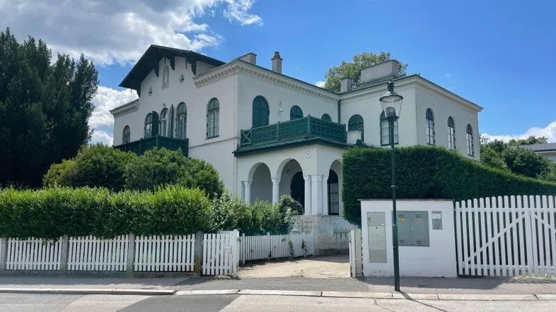 Elegante Villa mit weißer Fassade, grünen Fensterläden und gepflegtem Vorgarten.
