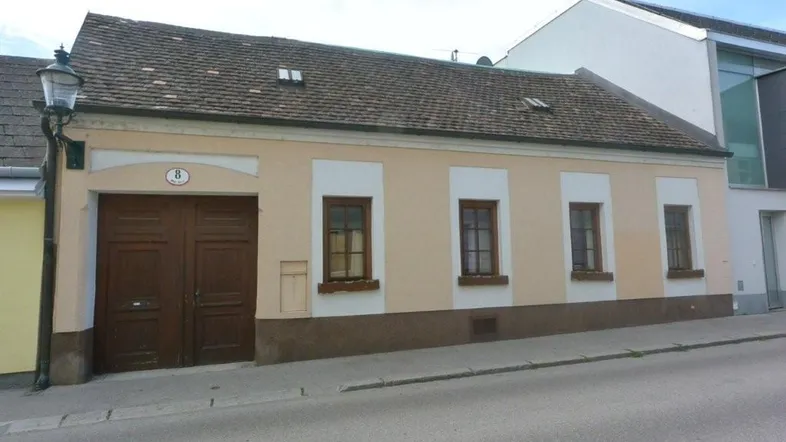 Traditionelles Haus mit beiger Fassade, braunen Holzfenstern und großen Holztüren an der Straße gelegen.