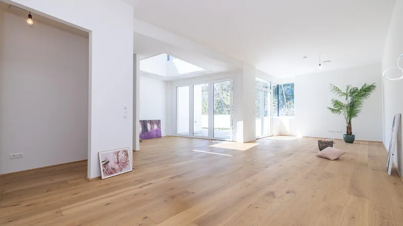 Helles, offenes Wohnzimmer mit Holzboden, großen Fenstern und viel Tageslicht.