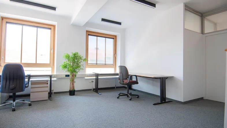 Helles und geräumiges Büro mit großen Fenstern, Teppichboden und modernen Deckenleuchten.
