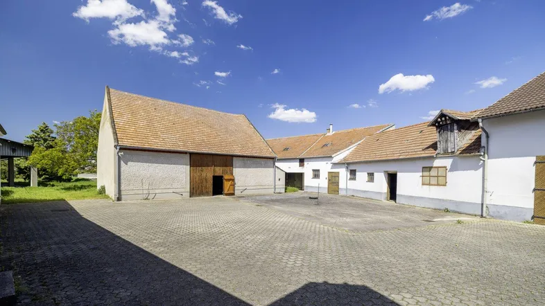 Großer gepflasterter Innenhof umgeben von traditionellen Gebäuden mit Scheunentoren unter blauem Himmel.