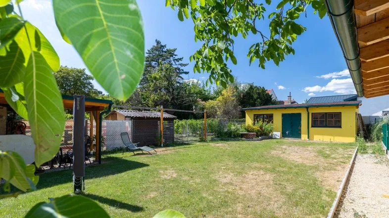 Weitläufiger Garten mit großer Rasenfläche und einem gelben Nebengebäude unter blauem Himmel.