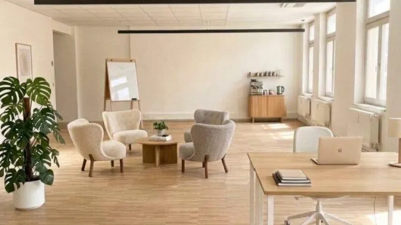 Großer, heller Büroraum mit Holzfußboden, großen Fenstern und verschiedenen Arbeits- und Sitzbereichen.