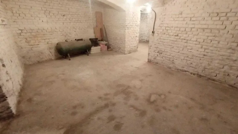 Geräumiger Kellerraum mit weiß gestrichenen Ziegelwänden, Betonboden und einem alten Tank.