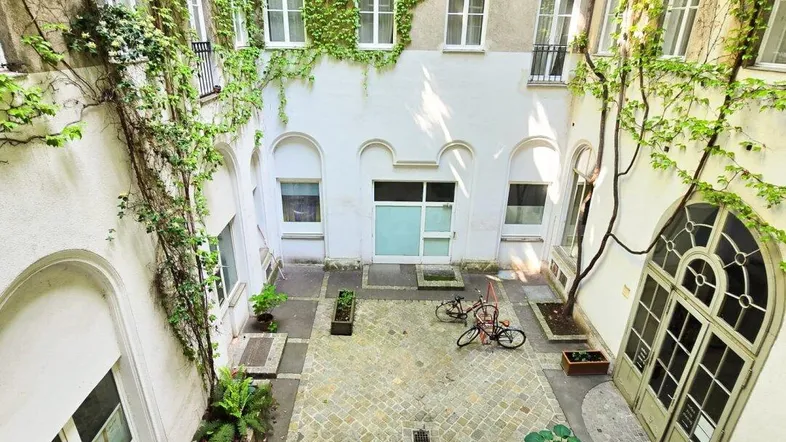 Begrünter Innenhof eines Altbaus mit Kopfsteinpflaster, vielen Fenstern und üppigem Efeu an den Wänden.