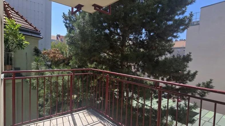 Heller Balkon mit Fliesenboden und Blick ins Grüne, umgeben von Bäumen.