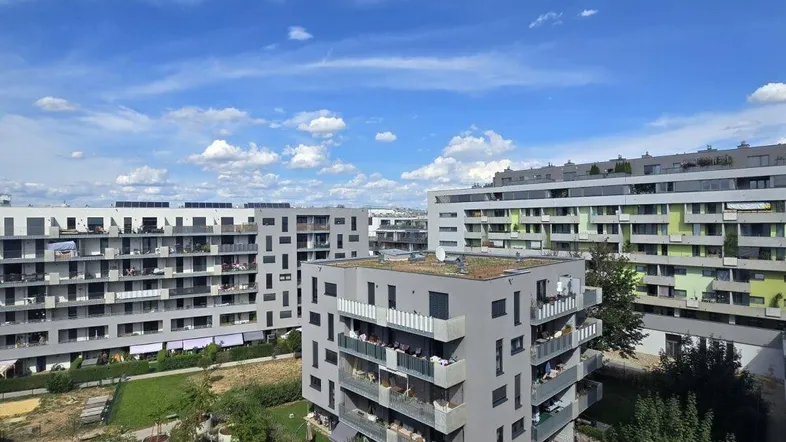 Weitläufige Ansicht moderner Wohngebäude mit begrünten Innenhöfen und blauem Himmel.