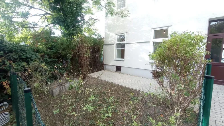 Kleiner Gartenbereich mit gepflasterter Terrasse und grüner Bepflanzung neben dem Gebäude.