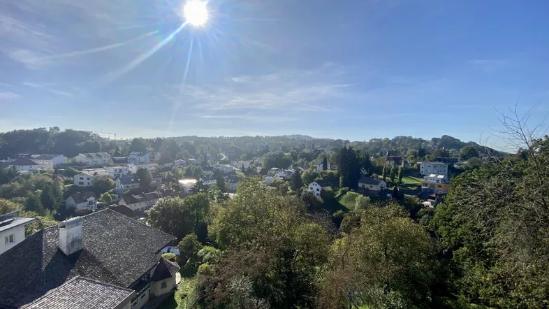 Panoramablick über die grüne Landschaft mit Häusern unter strahlendem Sonnenschein und blauem Himmel.