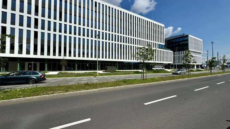 Modernes Bürogebäude mit markanter weißer Fassade und großen Fenstern entlang einer Straße unter blauem Himmel.