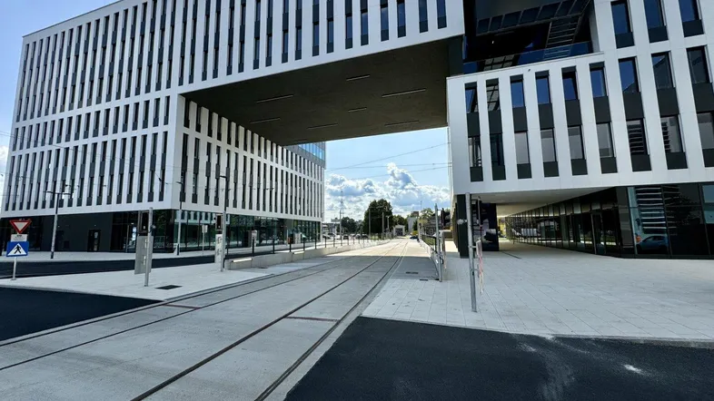 Modernes Bürogebäude mit markanter Überführung über die Straße, umgeben von städtischer Infrastruktur unter blauem Himmel.